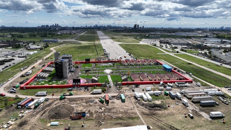 A drone photo shows a small community surrounded by a red wall with the city skyline in the distance. 